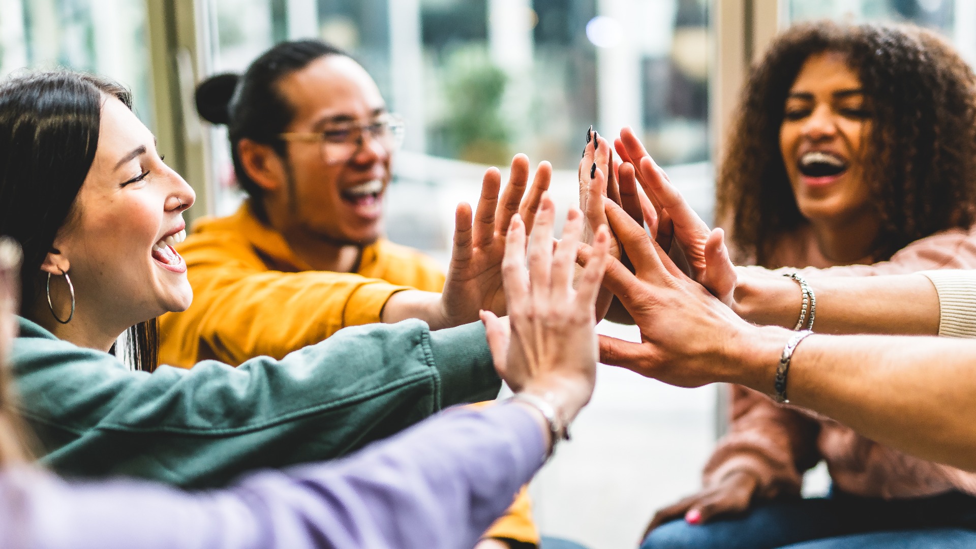 Multiracial happy young people stacking hands-Group of diverse friends  having fun unity together indoors at table of community-Human resources Concept Creative and Relationship Youth Culture